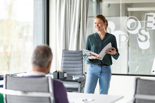 Smiling leader holding file folder talking with colleagues in workshop
