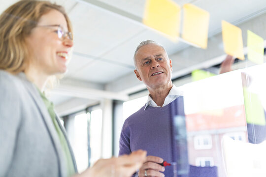Senior businessman discussing strategies on adhesive note with colleague at office