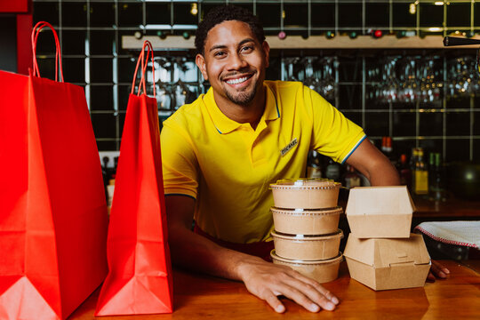 Smiling server at a restaurant counter with takeout food
