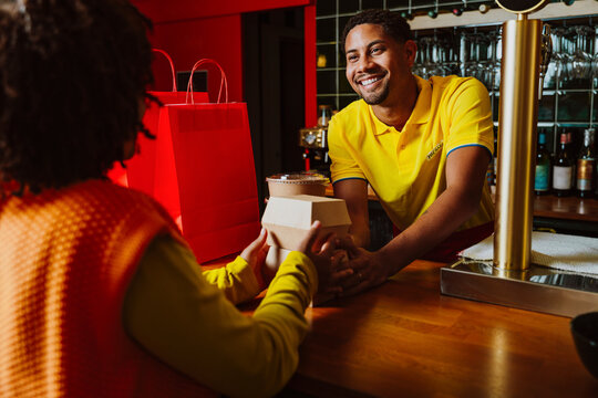 Smiling server handing takeout order to customer at restaurant counter