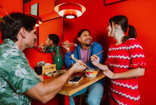 Friends smiling and eating sushi at a vibrant red restaurant
