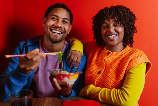 Smiling couple sharing a healthy poke bowl with chopsticks