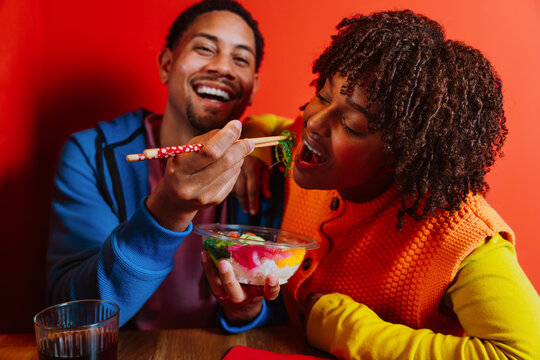 Smiling couple sharing healthy poke bowl indoors