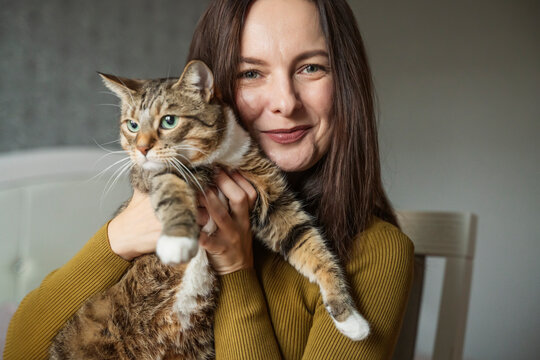 Woman smiling and holding a pet tabby cat at home