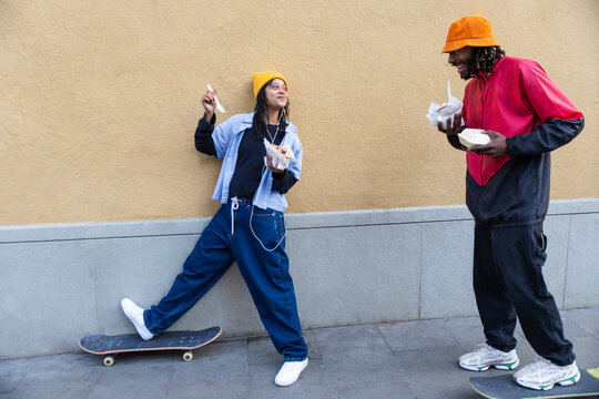Smiling skateboarders eating street food outdoors in the city