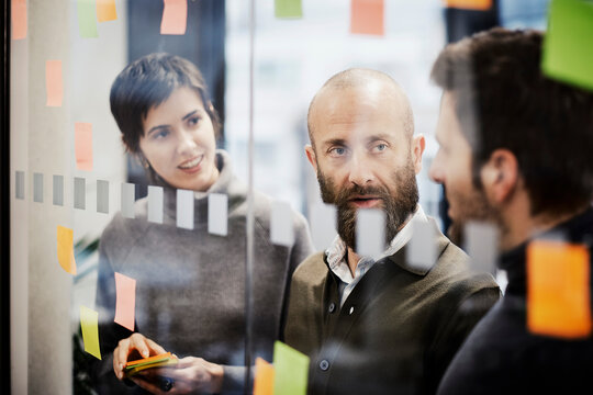 Mature businessman discussing ideas with coworkers near glass wall
