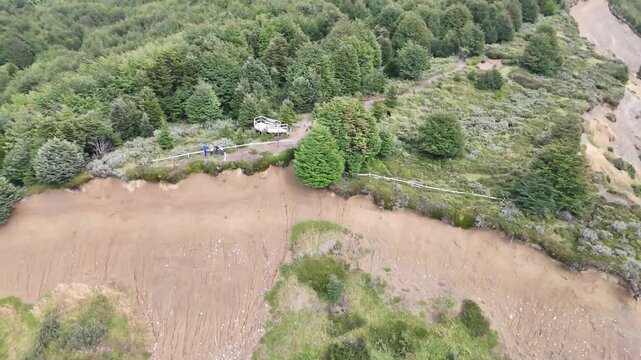 A cinematic drone shot moving forward over a dense subantarctic forest with a smooth pan down to reveal tourists at a fenced cliffside lookout point in Reserva Nacional Magallanes