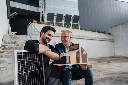 Engineers discussing a sustainable project with a model house and solar panel outdoors