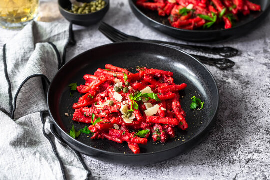 Beetroot casarecce pasta with capers and parmesan in a black bowl