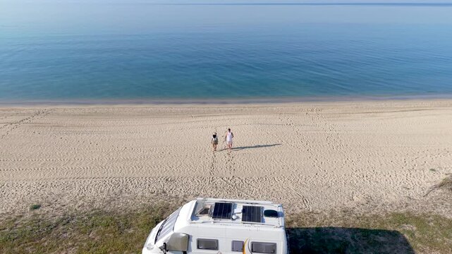 A couple experience serene moments on a pristine Chalkidiki beach in Greece, two travelers stroll along the shore, enjoying the warm sun and gentle waves. The camper van awaits nearby