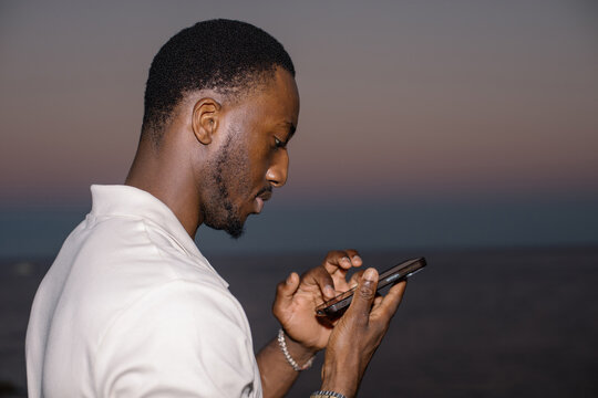 Man typing a text message on a smartphone outdoors at dusk