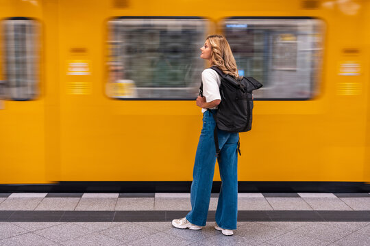 Woman with backpack waits for yellow train at subway station