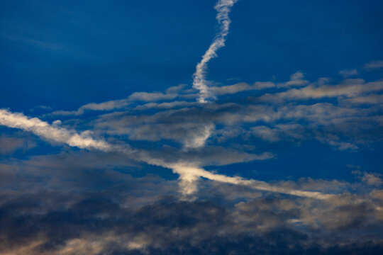 Intersecting airplane contrails in a blue sky with clouds in Austria