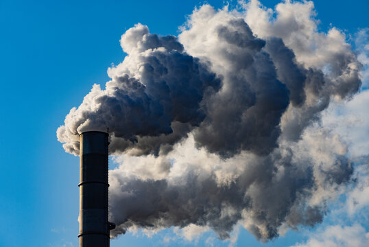 Thick smoke billowing from an industrial smokestack against blue sky