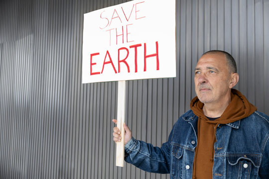 Man holding a save the earth protest sign outdoors in Barcelona