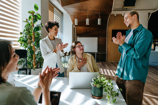 Colleagues applauding successful coworker in modern office meeting