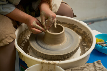 Fototapeta premium Close up of hands covered in wet clay molding a pottery vessel on a spinning wheel.
