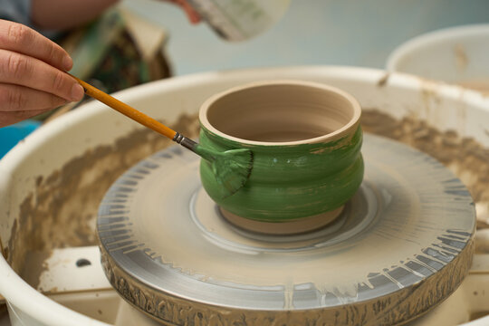 Fine arts studio photography of a potter glazing a round clay bowl with green wash.