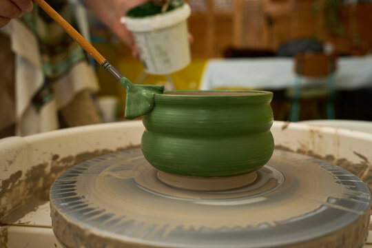 Artisan worker focusing on precision painting of a ceramic vessel with green tones.