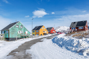Colorful wooden Inuit houses along a curving winter road with snowbanks, clear sky and arctic mountain scenery, Narsaq, Kujalleq, Greenland © vadim.nefedov