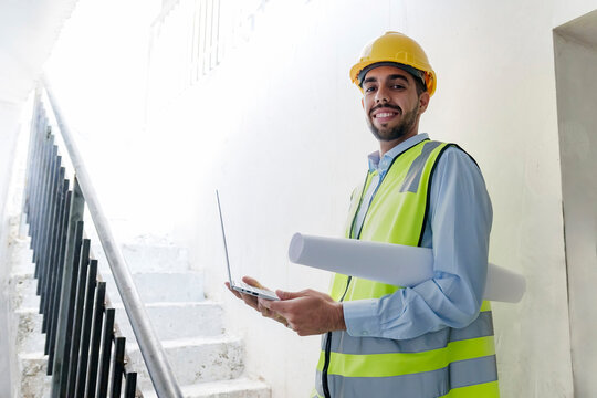 Smiling architect holding laptop at site