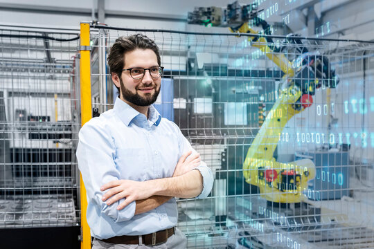 Smiling engineer standing with arms crossed near cage in factory