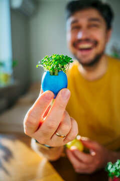 Hand holding a blue Easter egg with fresh healthy microgreens
