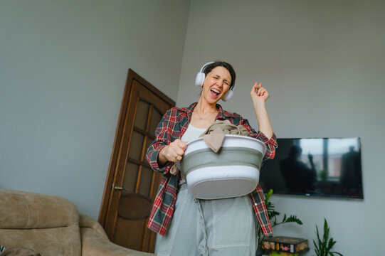 Happy woman listening to music while doing laundry and tidying up at home