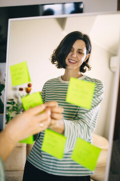 Woman smiling at mirror reflection with positive affirmation sticky note
