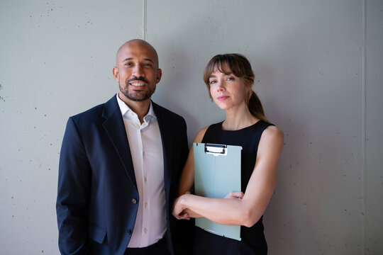Confident business partners standing indoors holding a clipboard