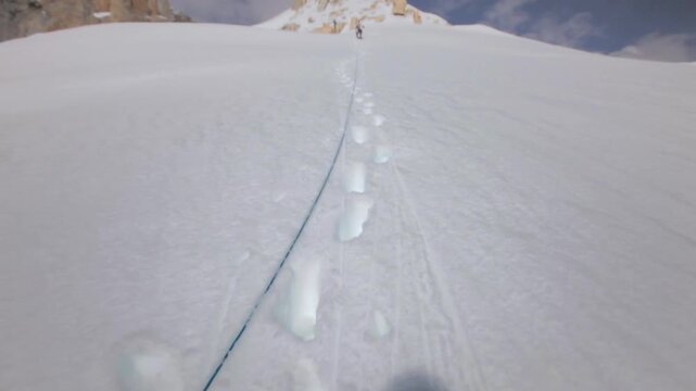 Point of view of a mountaineer abseiling down a steep, snow covered mountain face