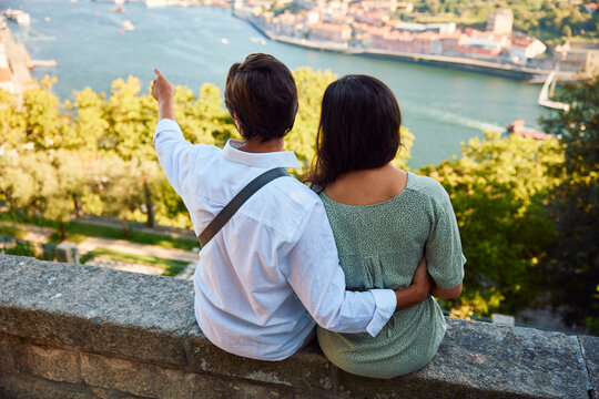 Young man gesturing with woman sitting in front of Douro river, Porto city in Portugal