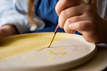 Obraz premium Professional ceramicist painting decorative motifs on a raw clay plate with yellow underglaze.