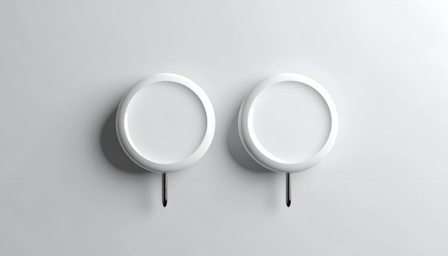 Two white, round objects with hooks, mounted on a white wall, minimal shadows