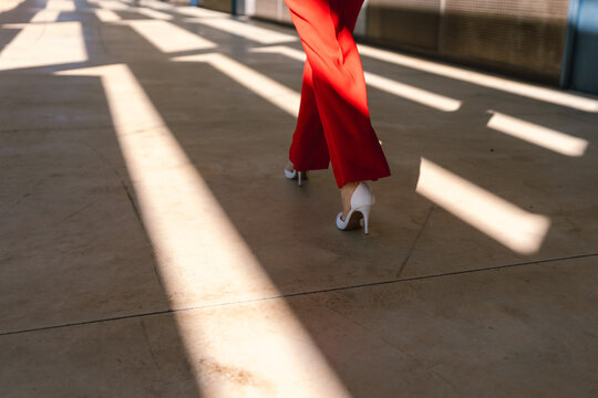 Legs in red trousers and high heels walking on sunny urban pavement