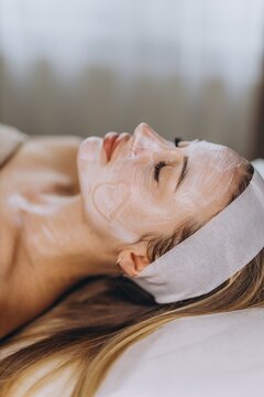 Spa client resting with facial skincare mask and heart shape indoors