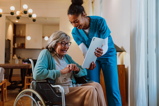 Nurse engaging with senior woman in wheelchair using tablet at home