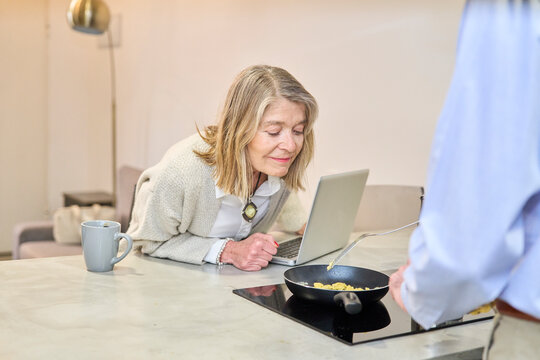 Couple prepares breakfast and uses a laptop at home indoors