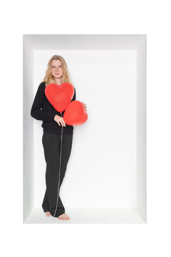Teenager holding heart shape balloons standing in alcove