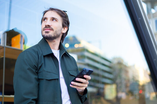 Architect holding smartphone and looking away outside