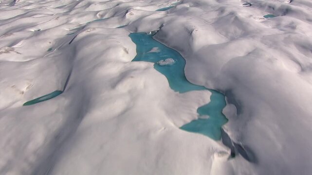 Aerial view of the melting ice cap in Greenland, revealing turquoise meltwater lakes and rivers