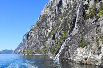 Beautiful waterfall Hengjanefossen cascading down steep dark granite cliffs covered with green trees into the Lysefjord, Norway. © Sheviakova