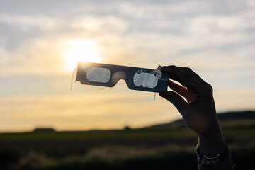 Hand holding protective solar eclipse glasses against a setting sun, safely observing an astronomical event © Víctor Sánchez