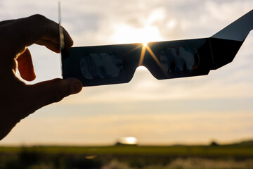 Hand holding solar eclipse glasses, sun shining through optical filters for safe celestial viewing © Víctor Sánchez