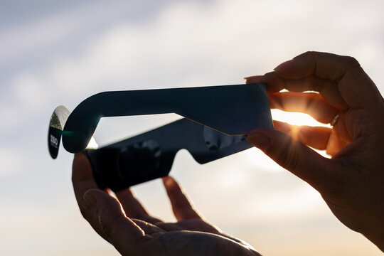 Hands holding solar eclipse glasses seeing bright sun rays during a celestial event for eye safety and protection