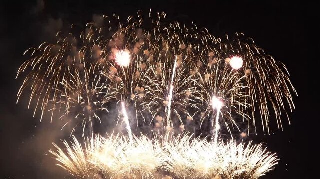 Bright golden fireworks exploding in the dark night sky during a celebratory event creating a cinematic visual display with brilliant sparks falling downwards in a beautiful slow motion video sequence
