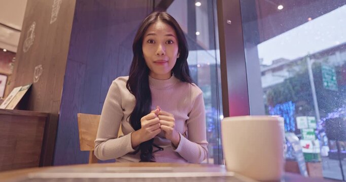 Beautiful young Asian woman with long black hair sits in a stylish coffee shop and gestures while chatting enthusiastically.
