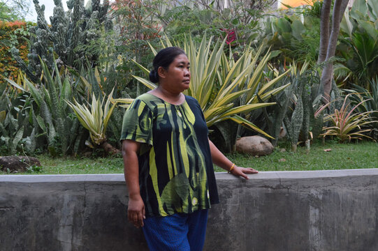 A woman looking sideways while resting her hand on a concrete border wall next to a garden filled with various agave and snake plants.