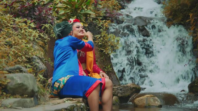 Man Fixing Woman's Hair Flower by Scenic Waterfall