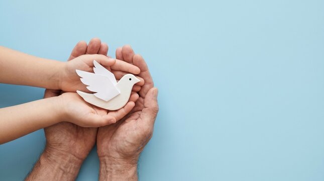 White paper dove in hands of adult and child, peace symbol for international day of non-violence, hope and harmony concept on blue background